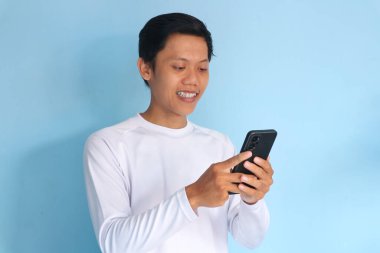 Genç Asyalı adam mutlu bir ifadeyle cep telefonuna bakıyor.