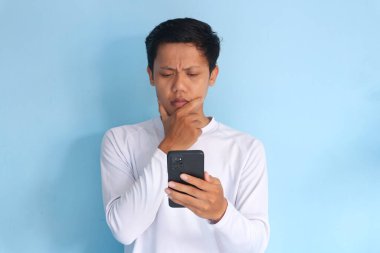 Genç Asyalı adam cep telefonu tutarken bir şeyler düşünüyor.