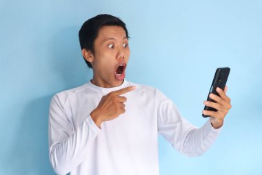 Genç Asyalı adam şok olmuş bir ifadeyle cep telefonuna bakıyor.