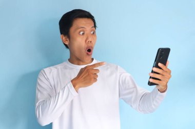 Genç Asyalı adam şok olmuş bir ifadeyle cep telefonuna bakıyor.