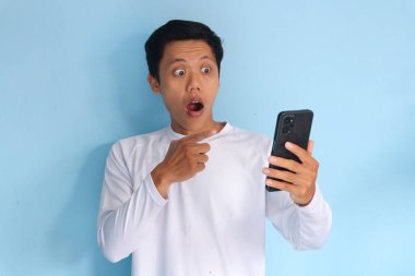 Beyaz tişört giyen Asyalı genç adam elinde cep telefonu tutarken şaşırdı.