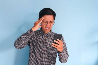 Cep telefonu tutan Asyalı genç adam mutlu bir ifade sergiliyor.