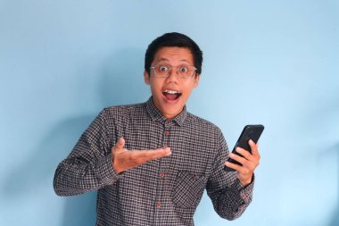 Genç Asyalı adam elinde cep telefonu tutarken inanılmaz bir ifade sergiliyor