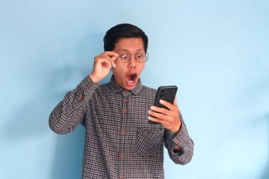 Genç Asyalı adam şok olmuş bir ifadeyle cep telefonuna bakıyor.