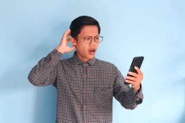 Genç Asyalı adam cep telefonunu karışık bir ifadeyle tutuyor.