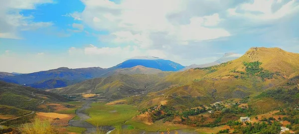 Vadinin kıyısındaki küçük bir köyün manzarası. Arka planda bulutlar ve sisle kaplı dağlar.