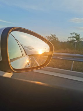 Aynadan gün batımını seyreden bir otoyolda araba sürüyor.