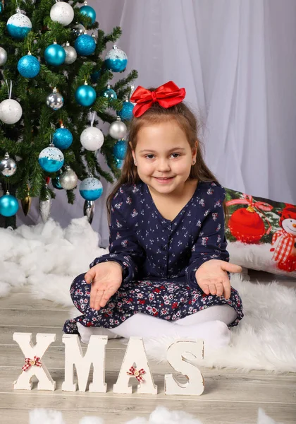 Süslü bir Noel ağacının önündeki mavi elbiseli küçük kız.