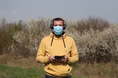 Bahar bahçesinde koruyucu maskeli genç adam elinde cep telefonu, Corona virüsü konsepti