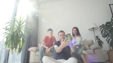 Mutlu aile, oturma odasındaki kanepede otururken akıllı telefondan selfie çekiyor. Akıllı telefondan aile fotoğrafı.