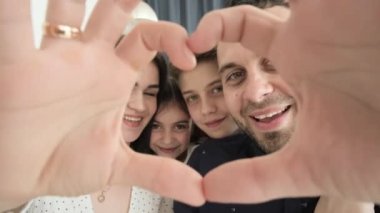 Büyük bir aile kalptir. Baba, anne ve kız kalp şeklinde el hareketi yapıyorlar. Aile kameraya bakıyor, gülüyor, aile sevgisi kavramını gösteriyor. Mutlu aile