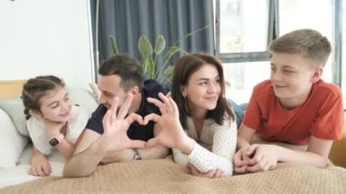 Büyük bir aile kalptir. Baba, anne ve kız kalp şeklinde el hareketi yapıyorlar. Aile kameraya bakıyor, gülüyor, aile sevgisi kavramını gösteriyor. Mutlu aile