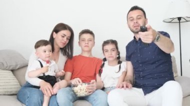 Büyük aile evde dinleniyor ve televizyon seyrediyor, anne, baba, küçük çocuklar komik film izliyor. Mutlu aile birlikte