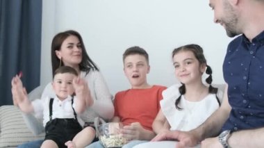 Büyük bir aile evde dinleniyor, anne baba küçük çocuklar küçük erkek kardeş küçük kız kardeş kanepede sarılıyor kameraya bak. Çocuklu bir çift kanepede dinleniyor.