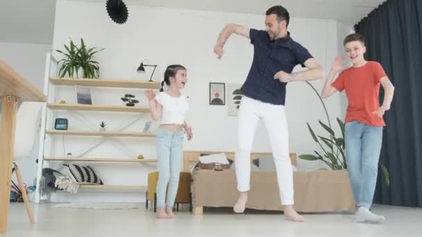 リビングルームで子供たちと一緒に踊る若いお父さん 自宅で休んで幸せな家族 彼らは楽しみを持っているとゲームをプレイ — ストック動画