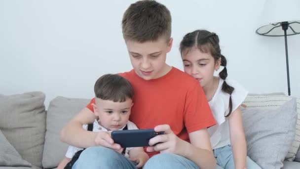 Çocuklar Evdeki Kanepede Otururken Akıllı Telefonla Oynuyorlar Ellerinde Bir Aletle — Stok video