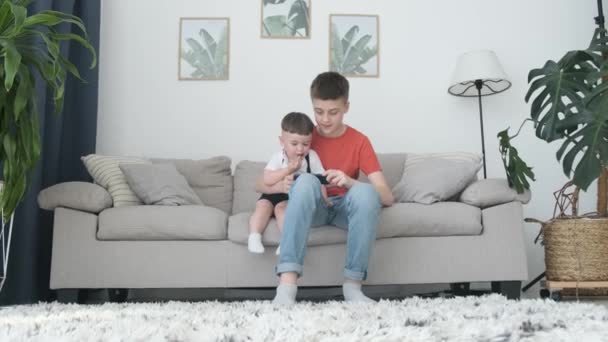 Zwei Brüder Spielen Hause Auf Dem Sofa Mit Einem Smartphone — Stockvideo