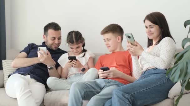 快乐的年轻家庭爸爸 妈妈和孩子们躺在柔软的沙发上 他们使用智能手机 享受放松 躺在舒适的沙发上 对互联网的依赖 — 图库视频影像