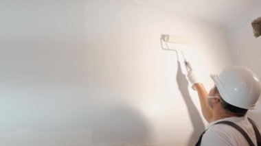 Evdeki modern tadilat, inşaat ve konsept. Duvarı silindirle boyayan bir adamın yakın çekimi. 4k video