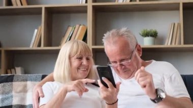 Mutlu emekliler kanepede dinleniyor ve modern akıllı telefon kullanıyor. Yaşlılar internet kullanıyor
