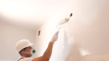 Genç bir adam ressam olarak çalışıyor. Yeni bir bina ya da apartman dairesinde duvarları silindirle boyuyor..