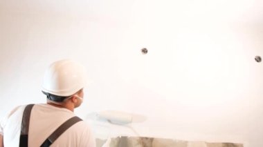 Erkek uzman, duvarları kapalı mekanla boyuyor, tamir konseptiyle. Kapalı alanda boya pateniyle çalışan yakışıklı genç bir inşaat işçisi..