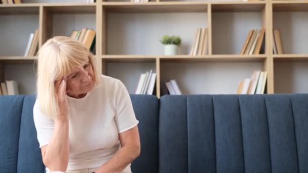 疲倦和偏头痛的老年妇女 一个退休的女人正坐在家里的沙发上 她很沮丧 — 图库视频影像