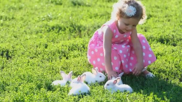 一个小女孩正和一只白兔在花园里玩耍 它坐在绿草上 夏天的一天 孩子们和宠物玩耍 这只宠物是一只白兔 — 图库视频影像