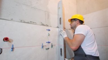 Sarı kasklı profesyonel bir mühendis inşaat çalışmalarının doğruluğunu kontrol ediyor. Seramik fayansların kurulumunun denetimi.