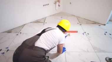 Profesyonel bir tiler su seviyesiyle çalışır. Bir adam fayans döşer. Ev yenileme konsepti. 4k