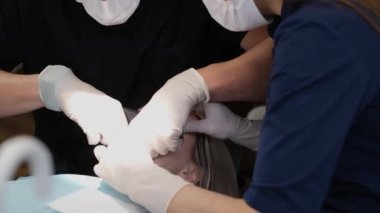 Maskeli dişçiler hastaların ağızlarını enstrümanlarla inceliyor. Bir dişçi ve asistanın işi. Sağlık ve Tıp Konsepti.