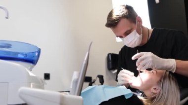 Profesyonel bir erkek dişçi kadın bir ziyaretçinin dişlerini muayene eder. Bir dişçi kliniğinde tedavi gören kadın bir hasta. Ağrısız diş tedavisi