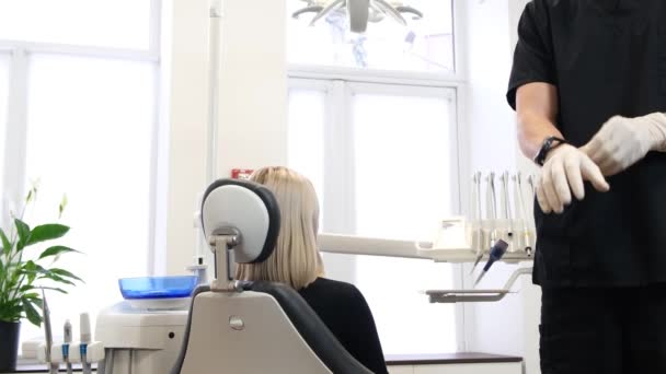 牙医准备检查病人 他戴上橡胶手套 一位妇女坐在牙医的椅子上 现代诊所的牙科治疗 — 图库视频影像