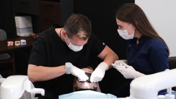 戴口罩的牙医用仪器检查病人的口腔 牙医和助理的工作 保健和医药概念 — 图库视频影像
