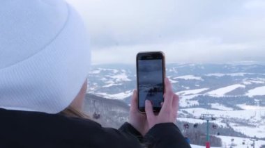 Kız akıllı telefondan karlı dağların arka planında video çekiyor..