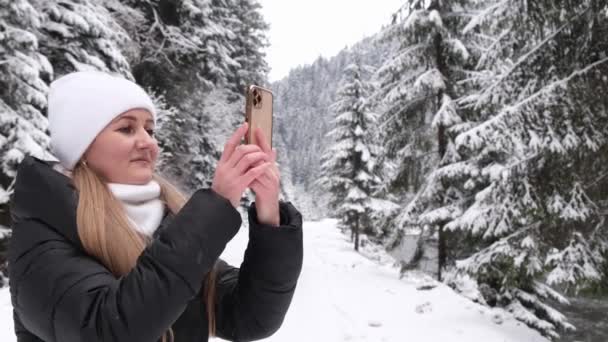 冬の森の中にスマート フォンで写真を撮る女の子 森を歩く婦人 — ストック動画
