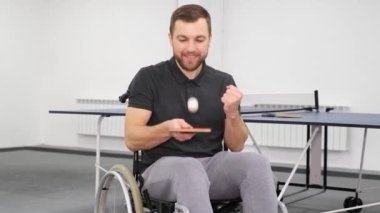 Tekerlekli sandalyedeki genç yakışıklı adam masa tenisi oynuyor. Engelli sporları