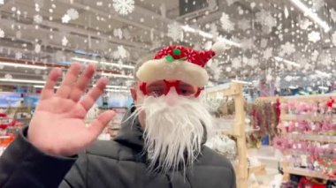 Noel Baba maskeli komik adam kameraya bakarken el sallıyor. Yeni Yıl ve Noel 2023 konsepti