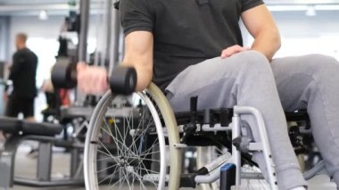 Tekerlekli sandalyede sakat bir adam spor salonunda dambıllarıyla egzersiz yapıyor..