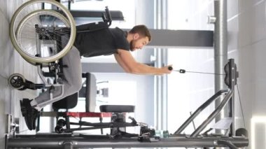Tekerlekli sandalyedeki engelli atlet spor salonundaki kol kaslarını eğitiyor, engelli insanlar spor yapıyor, dikey video çekiyor..