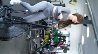 Sportif kız spor salonunda aeromotorla antrenman yapıyor. Spor yapan kız egzersiz bisikletinde kardiyo yapıyor. Dikey video