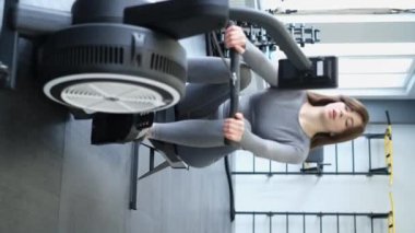 Spor salonunda kürek çeken bir kızın dikey videosu var. Sağlıklı yaşam tarzı. 4k video