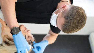 Dikey video. Bir doktor yaşlı bir kadını muayene eder ve estetik ameliyattan önce yüzünde izler bırakır. Blepharoplasty marka yakın plan.