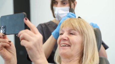 Trikolojistteki yaşlı bir kadın saçını profesyonel bir aletle inceliyor. Bir trikoloğun danışmanı.