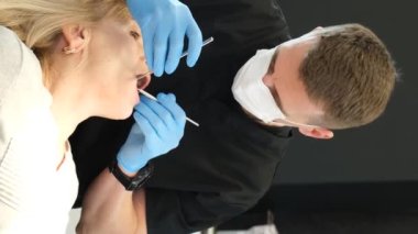 Bir dişçi eski dişlerin durumunu kontrol eder. Bir doktor sandalyedeki yaşlı bir kadının dişlerini muayene eder. Dikey video