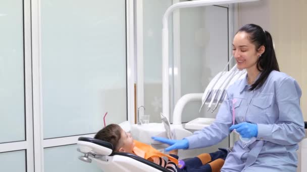 侧面视图的逗人喜爱的小男孩坐在牙科椅子上嘴巴张开 而牙医检查他的牙齿使用镜子在现代诊所 — 图库视频影像