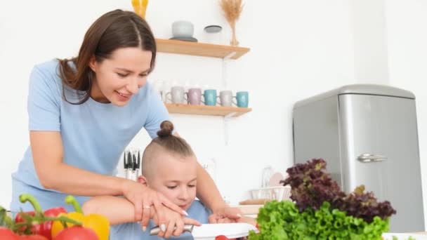 幸せな母親と彼女の小さな息子現代の白いキッチンで野菜料理を調理します おしゃれな髪型の男の子 — ストック動画