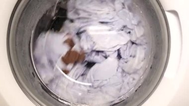 Kirli çarşafları yıkayan bir çamaşır makinesinin dönen davulunun yakın çekimi. Çamaşır makinesi operasyonu. 4k video