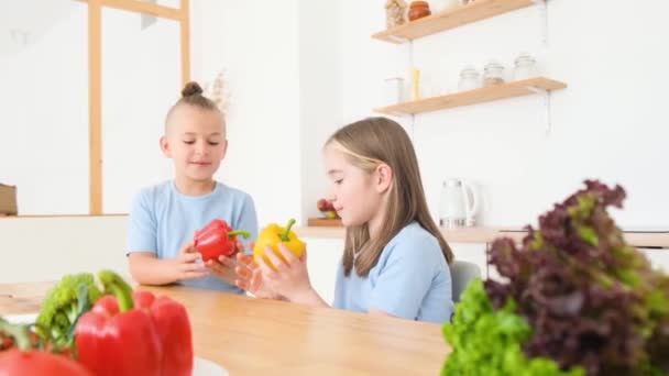 青いTシャツの弟と妹がキッチンに座って新鮮な野菜を食べています 幸せな子供の概念 子供の健康食品 — ストック動画