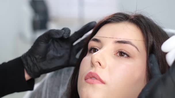 眉矯正手術中の女性メイクアップアーティスト プロの美容師だ 眉のねじ込みは 眉毛の形状を修正するための脱毛手順です — ストック動画